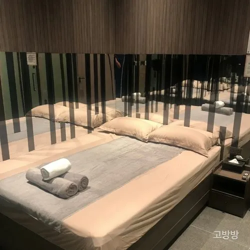 미러 헤드월과 우드 패널로 꾸민 샹핀 스파 객실의 넓은 침대와 타월, 마카오